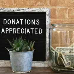A donation jar with cash in it next to a sign that reads Donations Appreciated