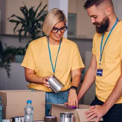A woman and man in matching volunteer t-shirts packing food into boxes